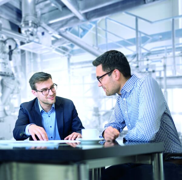 Two men in conversation at a table, discussing documents in a modern office